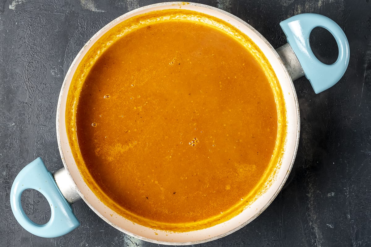 将番茄汤与胡萝卜和洋葱混合在一个深色背景的平底锅里。