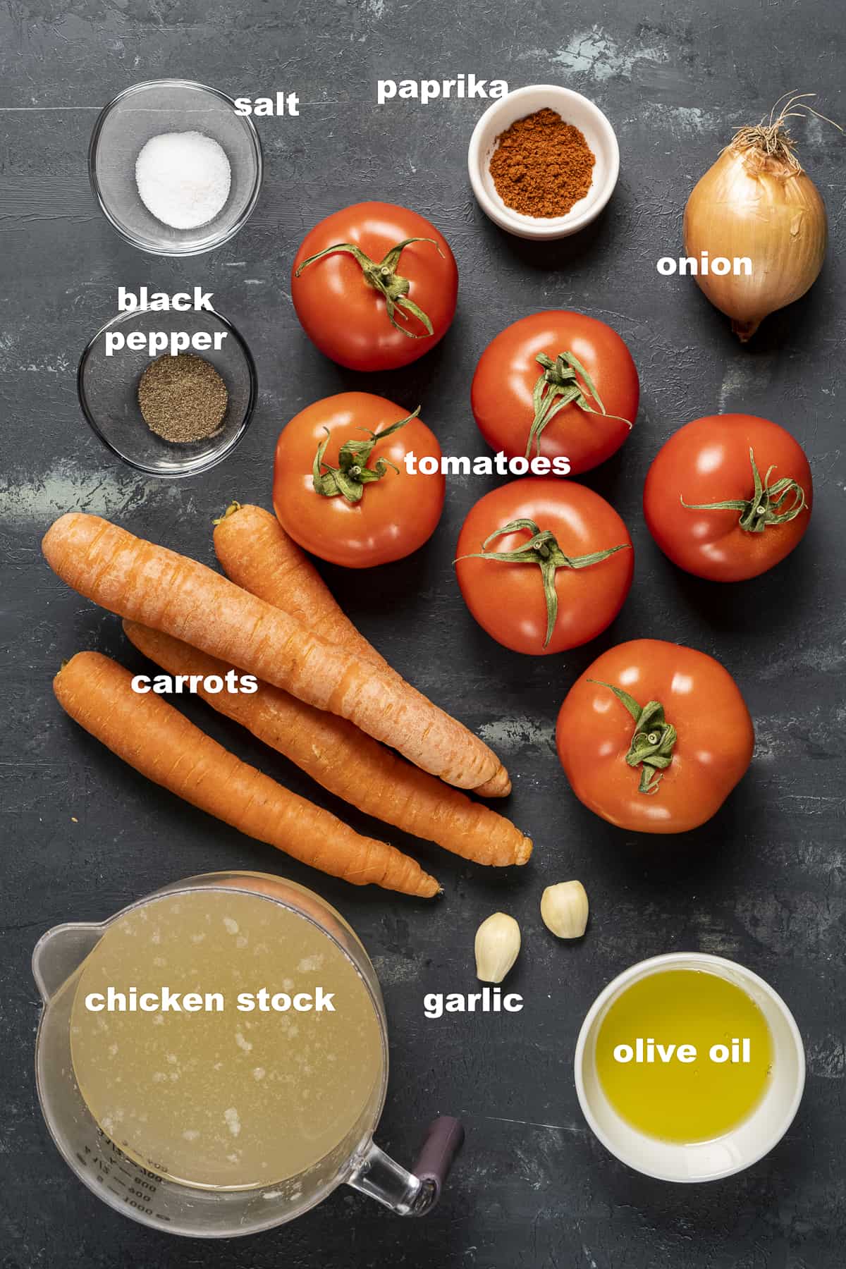 把西红柿、胡萝卜、鸡汤、橄榄油、大蒜、洋葱、盐、胡椒粉和辣椒粉放在深色的背景上。