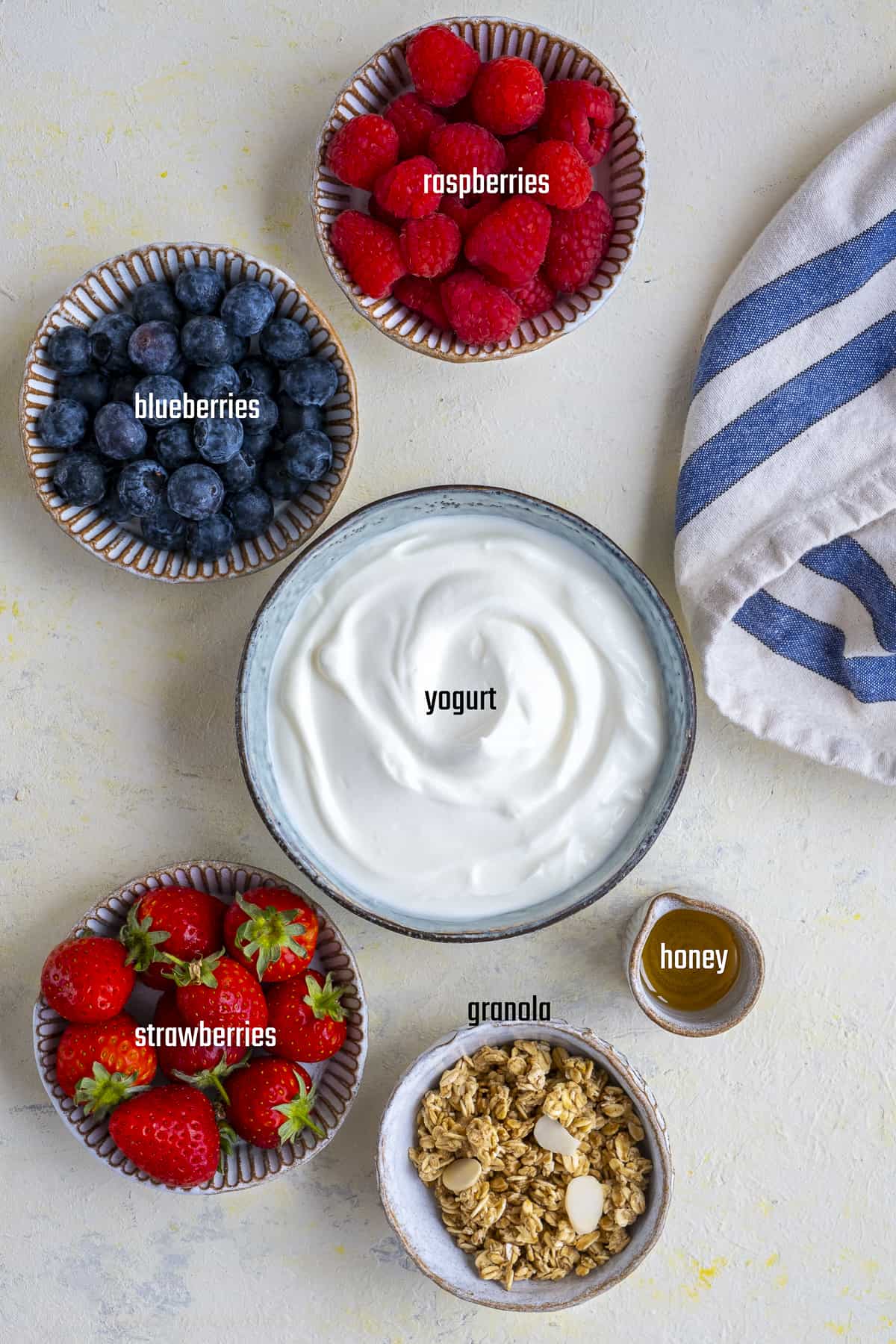 酸奶，覆盆子，蓝莓，草莓，格兰诺拉麦片和蜂蜜放在不同的碗里，背景淡一点。