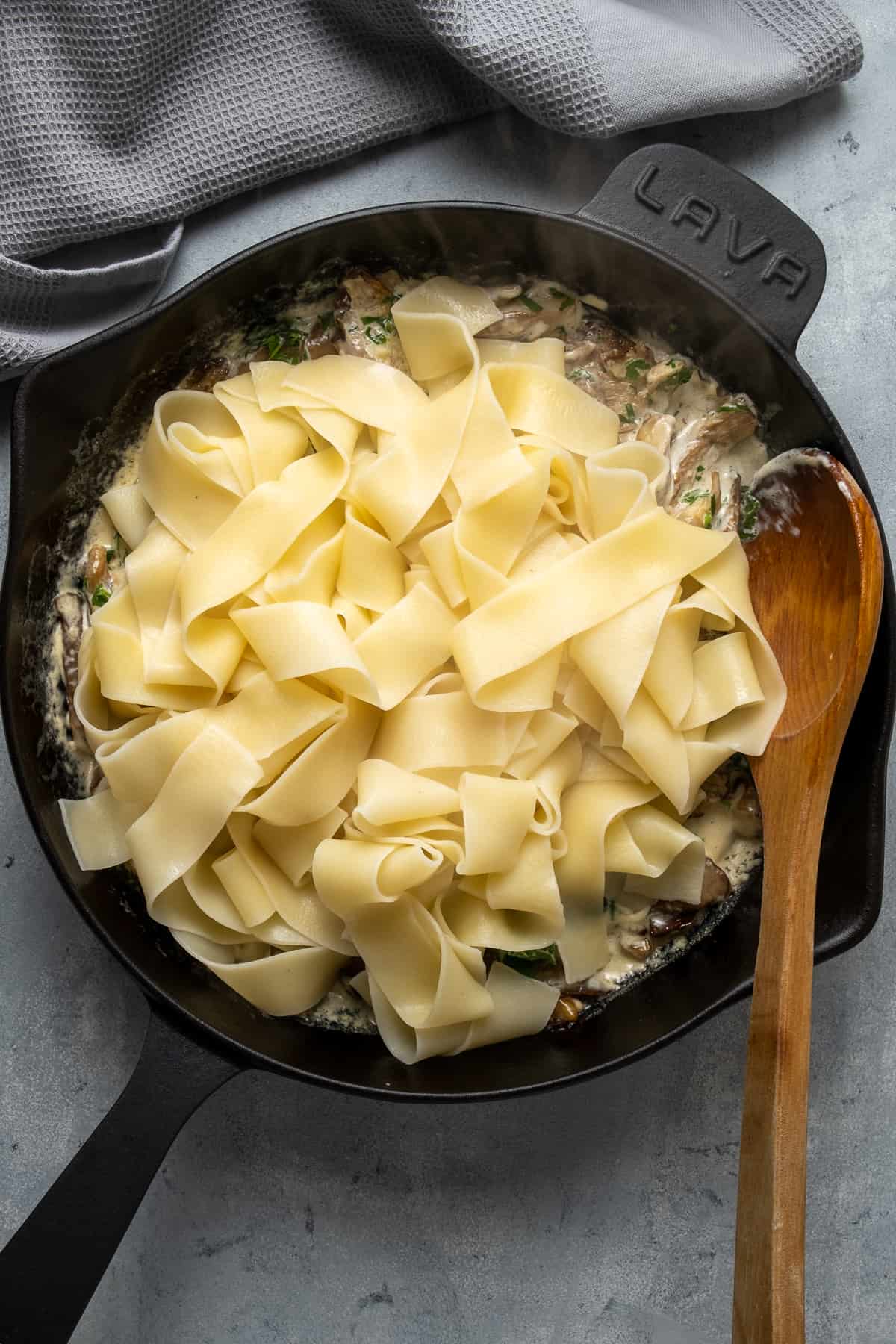 煮熟的意大利面和奶油蘑菇酱在铸铁煎锅和木勺里面。