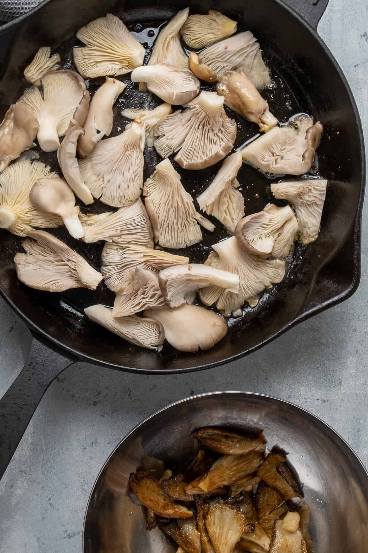 在铸铁煎锅里煎的平菇和一些煎过的平菇放在旁边的碗里。