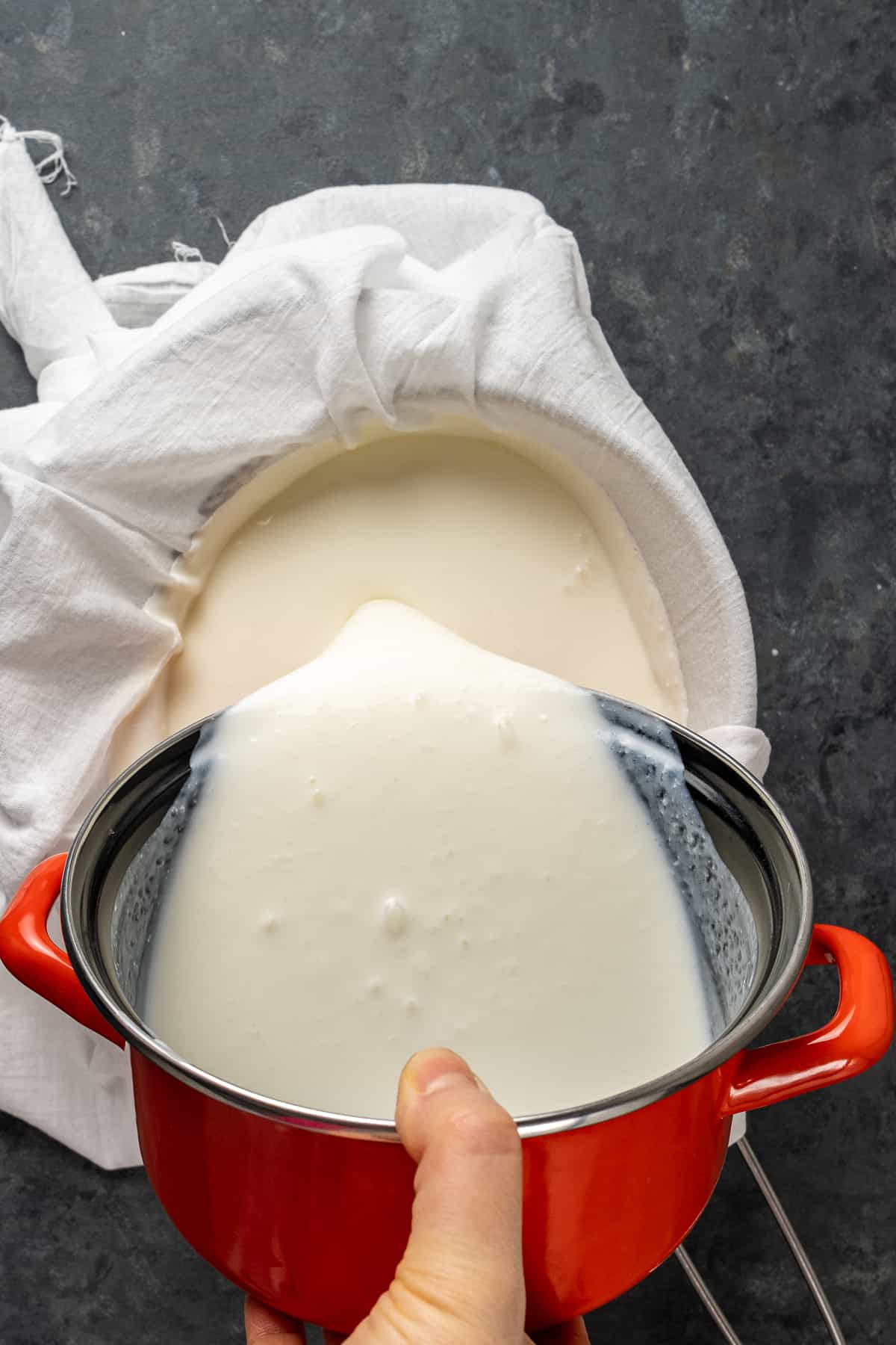 一只手从一个红罐子里倒酸奶到一块白色的薄纱上。