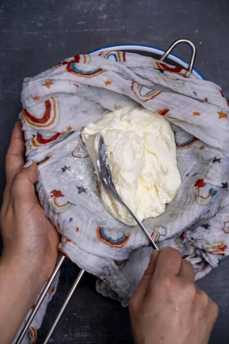 双手用勺子在小棉布上检查过滤酸奶的粘稠度。