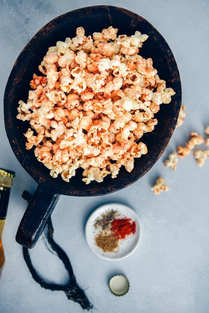 Homemade stovetop popcorn seasoned with chili powder, black pepper and cumin. #spicypopcorn #homemadepopcorn #howtomakepopcorn 麻辣的爆米花装在一个大木碗里,小盘子里装着香料。