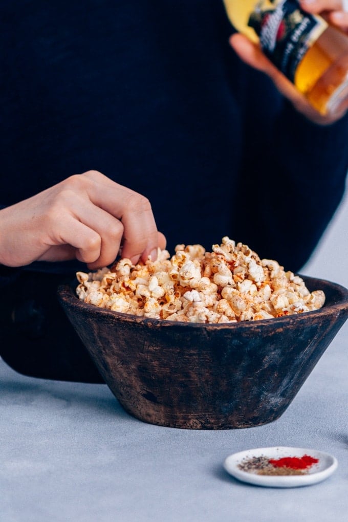 Homemade stovetop popcorn seasoned with chili powder, black pepper and cumin. #spicypopcorn #homemadepopcorn #howtomakepopcorn 女人吃着碗里的辣爆米花,喝着啤酒。
