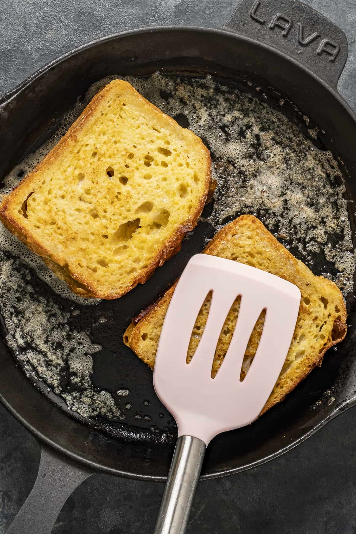 用锅铲压在煎锅里的面包片上。