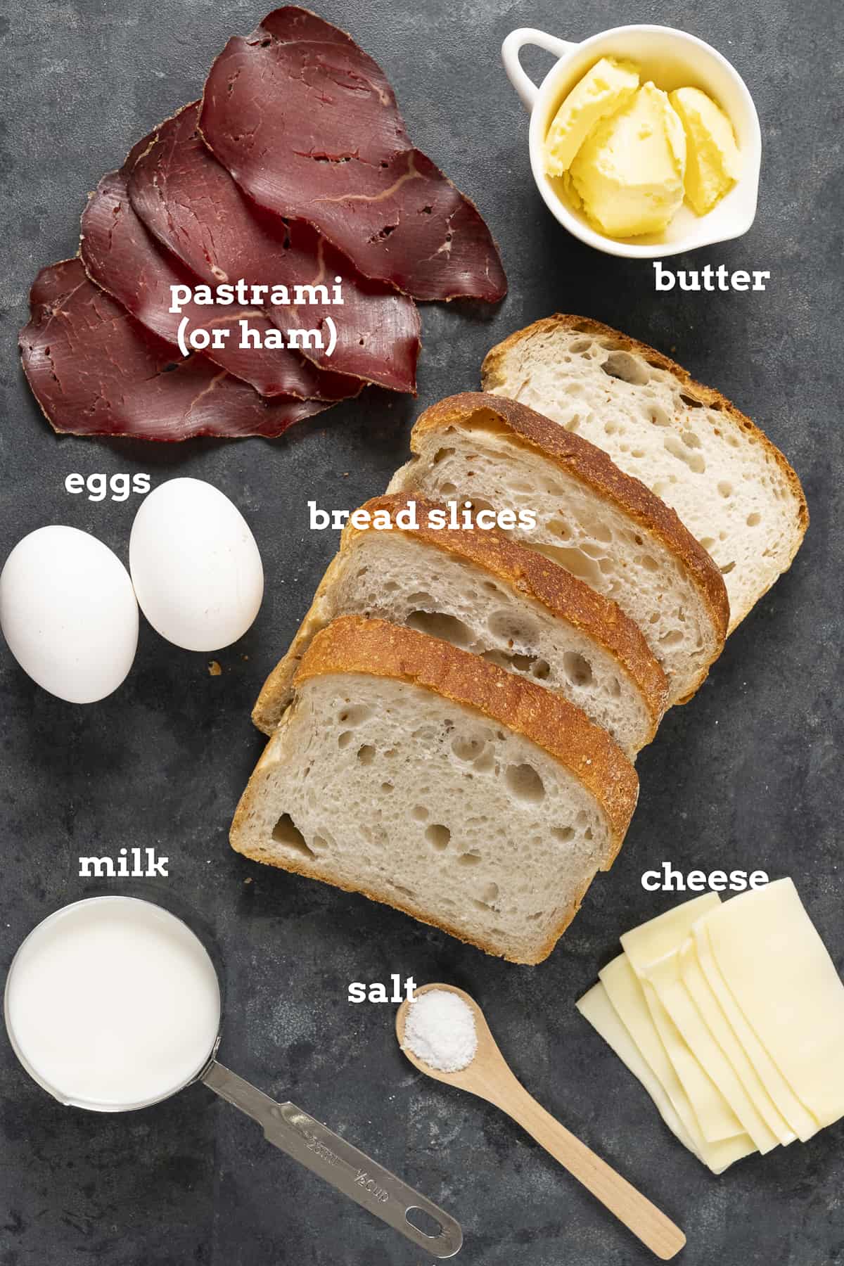 鸡蛋、冷肉片、黄油、面包片、奶酪片、牛奶和盐放在深色背景上。