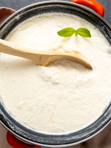 用一个木勺在搪瓷罐里自制酸奶，上面放一根新鲜的薄荷。