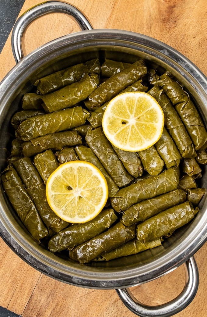 Dolmades with lemon slices on the top in a pot.
