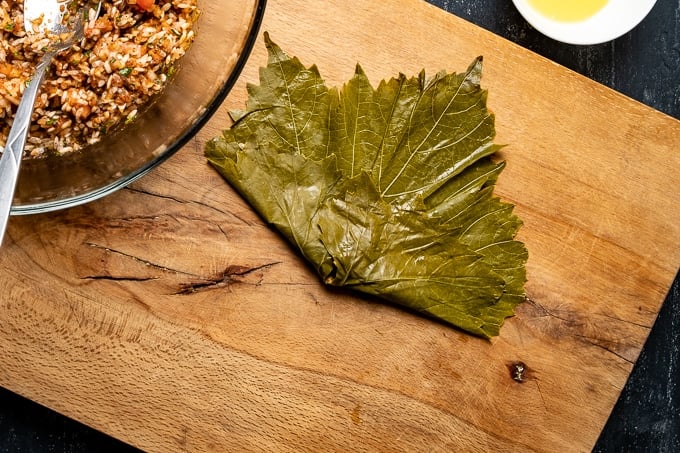 A grape leaf is stuffed with rice and folded on a wooden board.