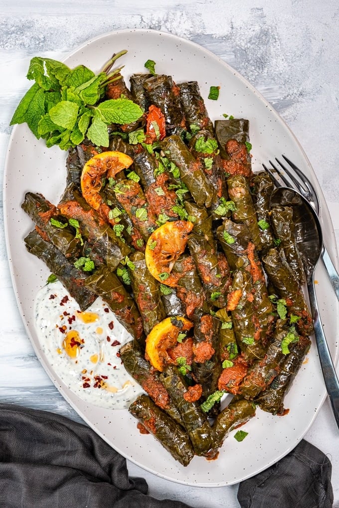 Stuffed grape leaves yaprak sarma with tomato sauce and lemon wedges on the top served on a white oval plate.