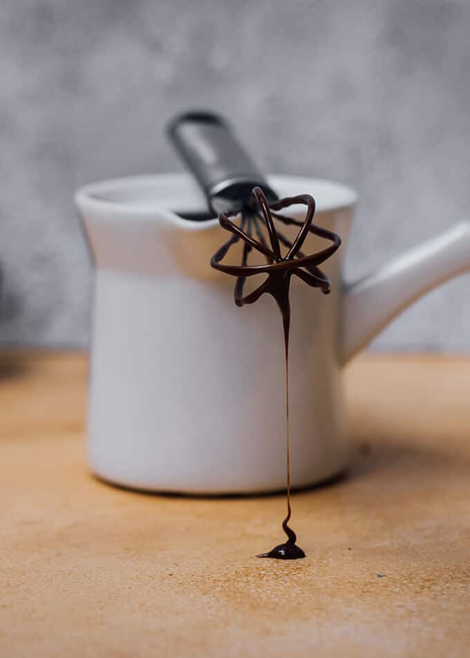 巧克力甘纳许从一个小的手打器滴在陶瓷咖啡壶上。