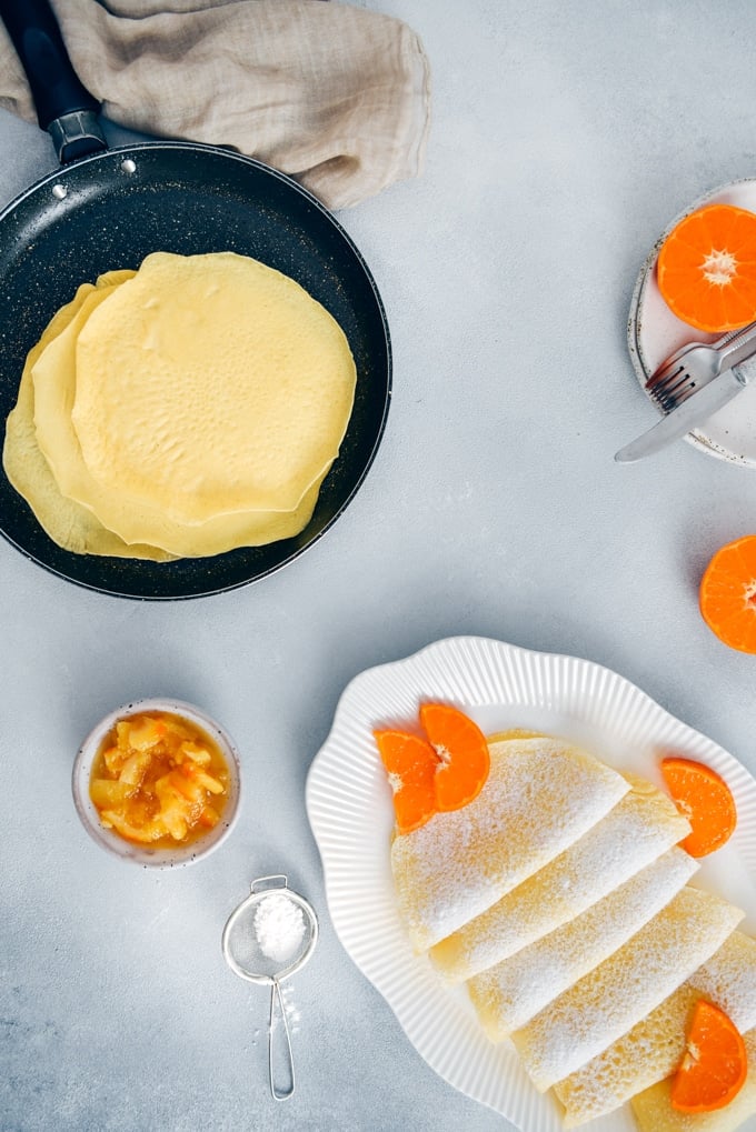 Wonderfully thin gluten free crepes made with rice flour are no different from regular crepes! So easy to make with only 4 simple ingredients. Perfect for several filling options! #glutenfreebreakfast #glutenfreecrepes #riceflourrecipes 米粉法式薄饼配上橙色片和糖粉。