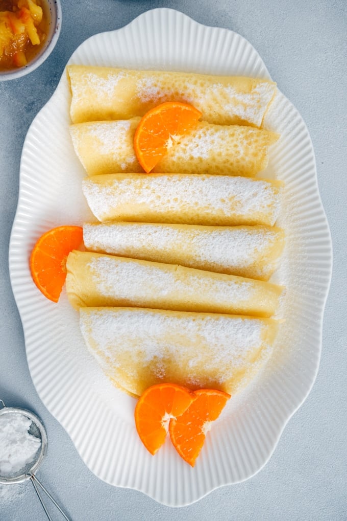 无谷蛋白法式薄饼在白色椭圆盘,点缀以橙片和糖粉。