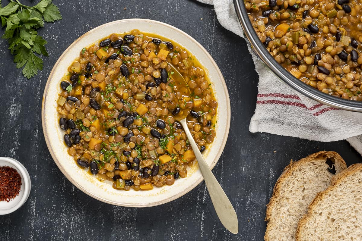 Black bean lentil soup served in a white bol, some bread, parsley and red pepper flakes on the side.