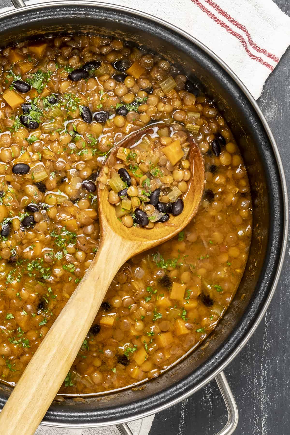 Black bean soup with lentils and vegetables in a pot and a wooden spoon in it.