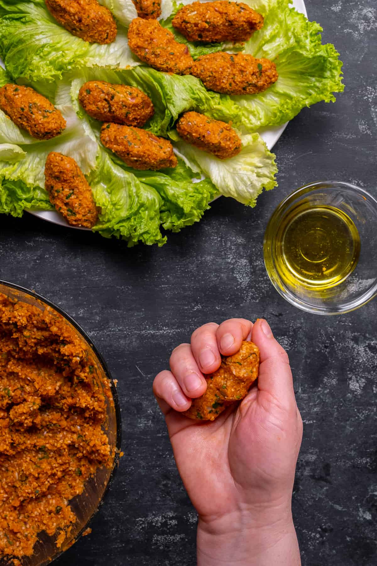 Mercimek koftesi正在成形,更多的扁豆球和一小碗橄榄油在旁边。