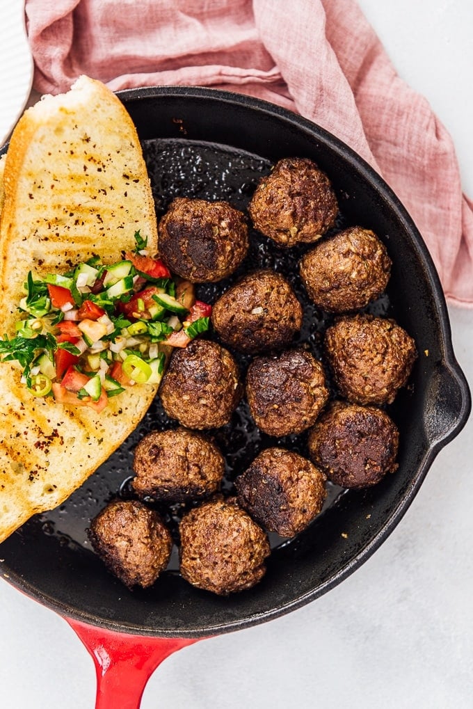 Homemade Turkish Meatballs are spicy, tender and perfectly juicy. It’s not a secret any more to make meatballs at home. #turkishfood #meatballs #meatballsrecipe #middleeasternfood #kofta #kofte 土耳其肉丸和一片烤面包,上面撒着沙拉,放在铸铁锅里。