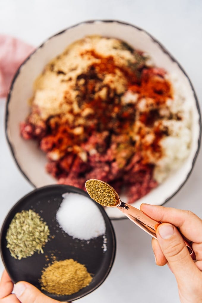 Homemade Turkish Meatballs are spicy, tender and perfectly juicy. It’s not a secret any more to make meatballs at home. #turkishfood #meatballs #meatballsrecipe #middleeasternfood #kofta #kofte 手用铜勺将香料洒在盛在陶瓷碗里的食材上。