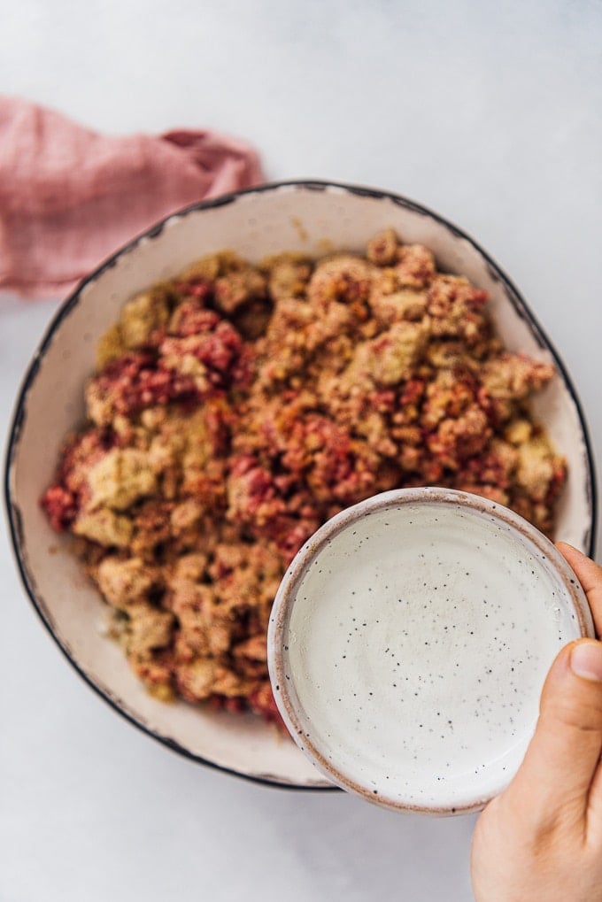 Homemade Turkish Meatballs are spicy, tender and perfectly juicy. It’s not a secret any more to make meatballs at home. #turkishfood #meatballs #meatballsrecipe #middleeasternfood #kofta #kofte 一只手从一个迷你陶瓷碗里倒水浇在鱼丸的配料上。