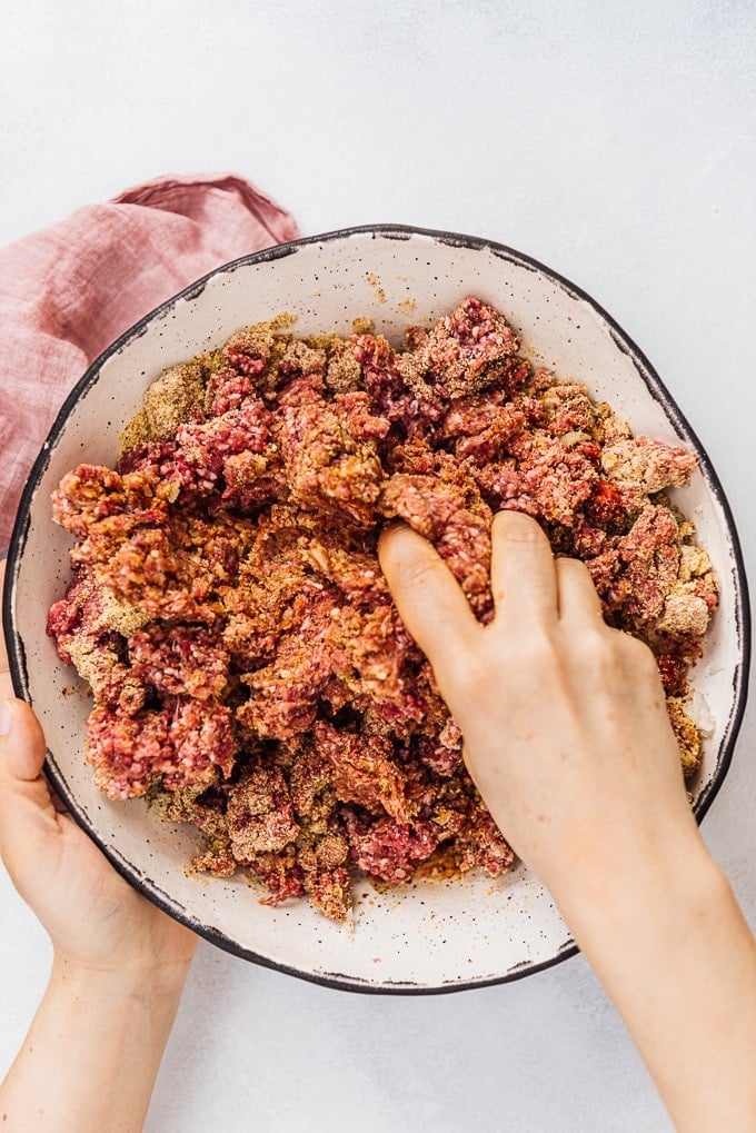 Homemade Turkish Meatballs are spicy, tender and perfectly juicy. It’s not a secret any more to make meatballs at home. #turkishfood #meatballs #meatballsrecipe #middleeasternfood #kofta #kofte 双手在陶瓷碗里搅拌土耳其肉丸。
