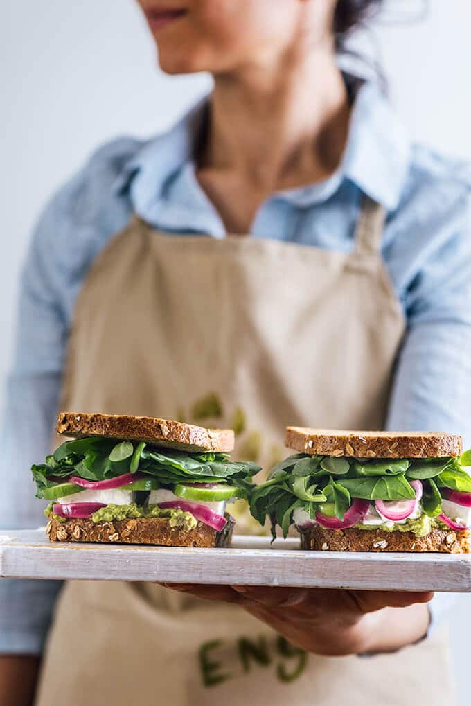 Cold cheese sandwich with avocado, cucumbers and herbs. Homemade quick onion pickles recipe is included. #cheesesandwich #sandwichrecipe #breakfastsandwich #lunchsandwich 一名妇女在上奶酪和泡菜三明治,里面放满了香草