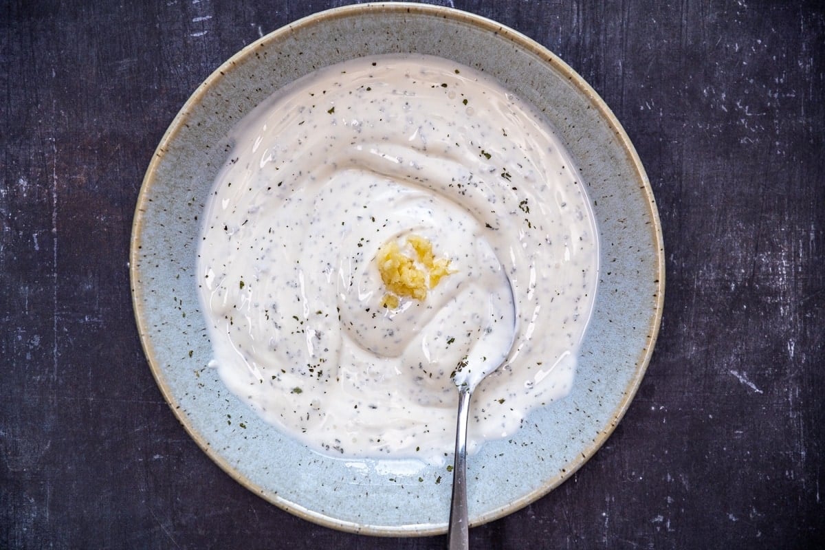 把蒜泥和酸奶、盐、干薄荷混合在一个蓝色的碗里，把勺子放在里面。