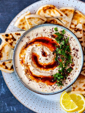正宗的Hummus在一个碗里搭配辣椒粉油，Sumac和欧芹。鞋面面包块和柠檬楔子在一边。
