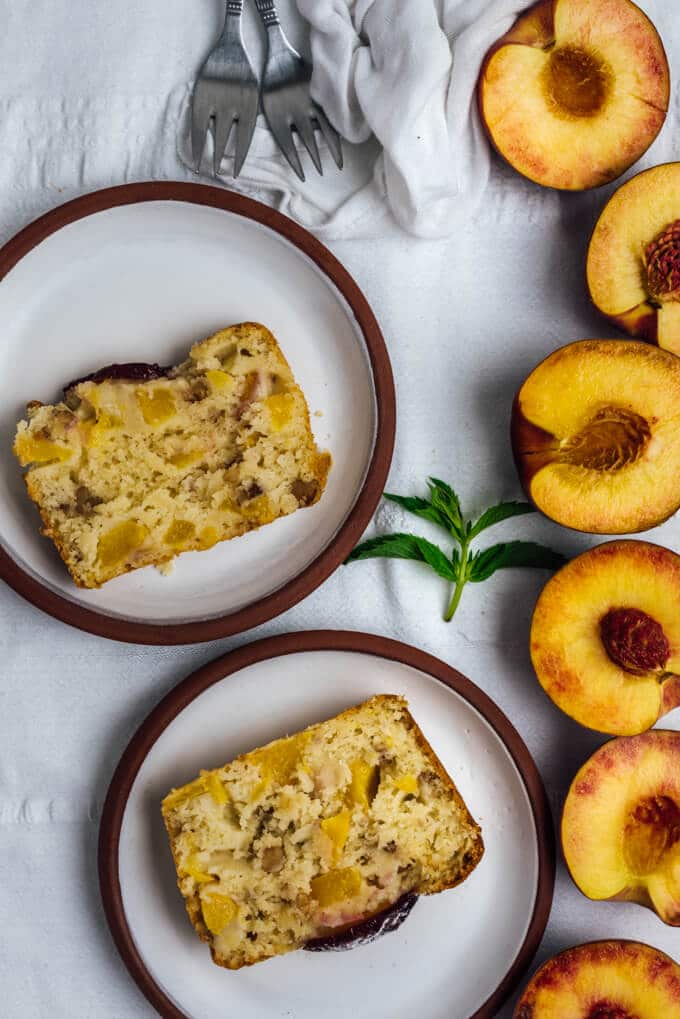 Peach Bread with Walnuts is wonderfully moist and flavorful thanks to fresh peach chunks and cinnamon on its top. #peach #loafcake #peachrecipe #peachbread 白色陶瓷盘子上的桃子面包片
