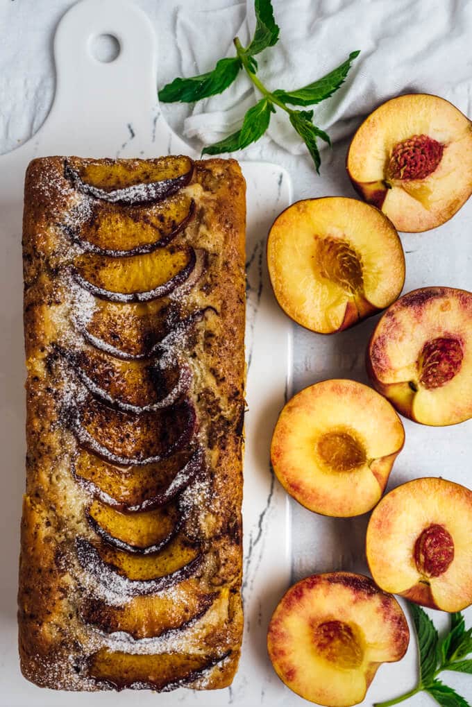 Peach Bread with Walnuts is wonderfully moist and flavorful thanks to fresh peach chunks and cinnamon on its top. #peach #loafcake #peachrecipe #peachbread 白色砧板上的新鲜桃片面包