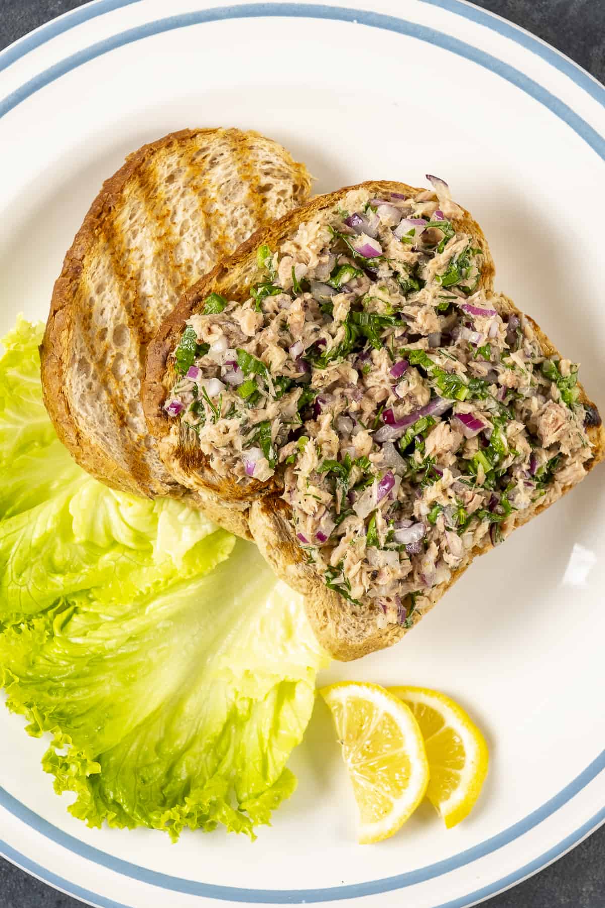 金枪鱼沙拉夹在烤面包片上，配以生菜叶和柠檬角。