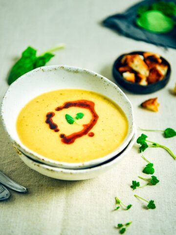 土耳其红扁豆汤，淋上辣椒油，放在一个白色的碗里，配上香草和油炸面包丁。