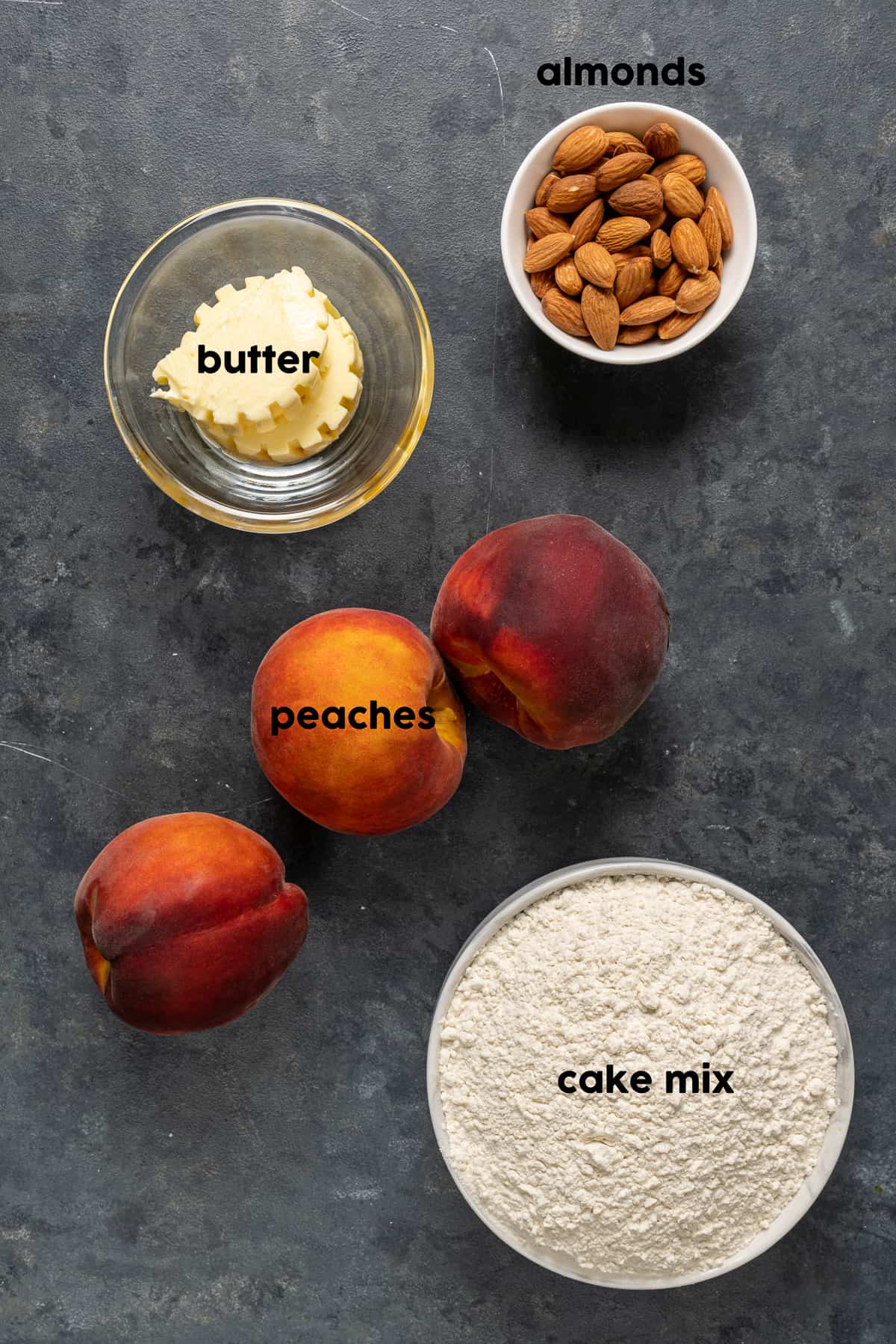 把桃子、黄油、杏仁和一碗蛋糕粉放在黑色的背景上。