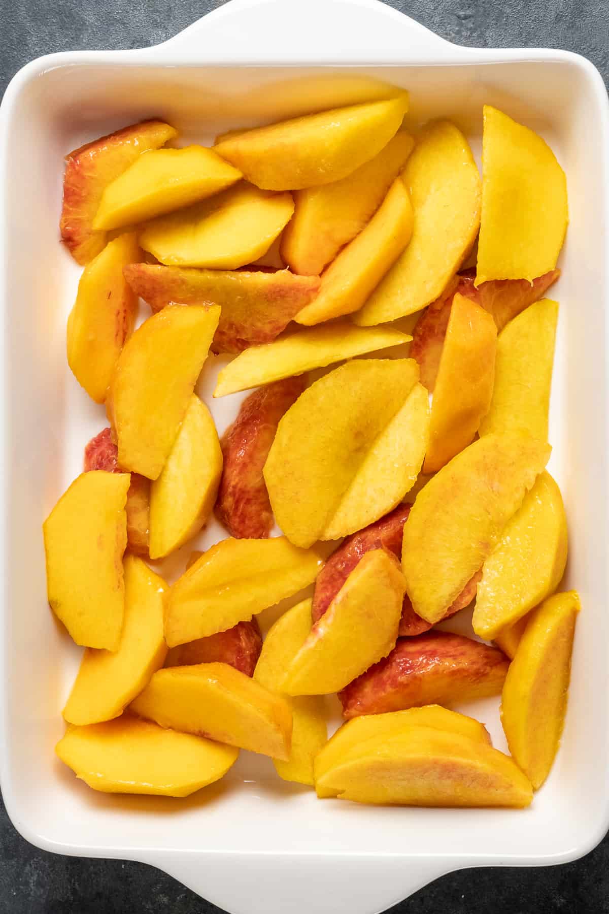 桃子片覆盖在白色矩形烤盘底部。