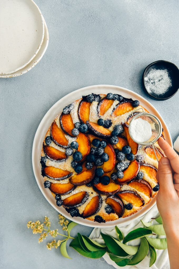 This Blueberry Peach Coffee Cake is a luscious cake that is sure to be a crowd pleaser. Made with olive oil and kefir, this simple cake is moist, tender and so light. #peachcake #peachcoffeecake #peachrecipe #coffeecake #kefircake #kefirrecipes 将糖粉筛在桃子咖啡蛋糕上,配上新鲜的桃子