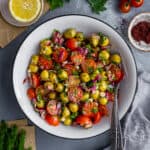 Green olive salad with tomatoes, onions and herbs in a white bowl and two forks inside it.