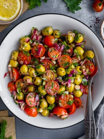 白碗里放着番茄、洋葱和香草的绿橄榄沙拉，里面放着两把叉子。