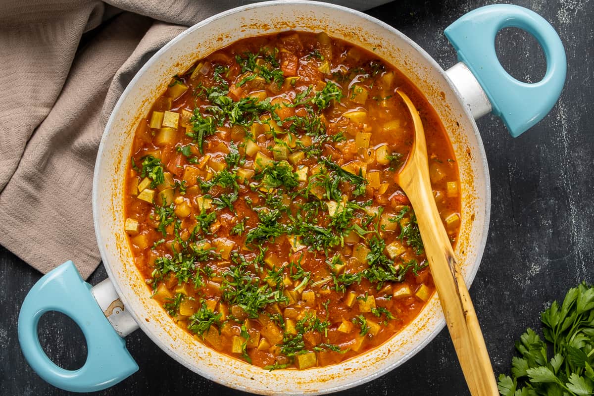 西葫芦番茄炖菜，上面撒上切碎的欧芹，平底锅里放一把木勺。
