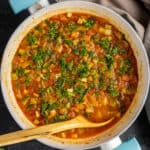 Zucchini stew with tomatoes and herbs in a white pan and a wooden spoon in it.