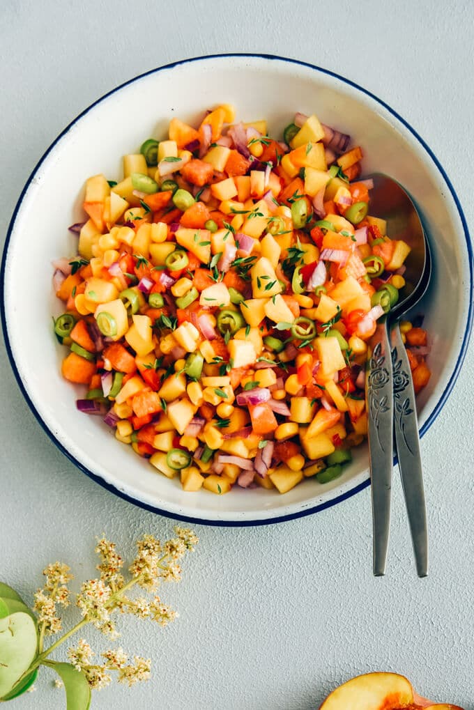 Fresh Corn Peach Salsa is a great recipe to bring summer on your table. Thanks to tangy garden tomatoes, hot peppers and red onion, this is not an overly-sweet salsa. Perfect on chips, chicken, fish or even in sandwiches. #salsa #peachsalsa #salsarecipe #freshpeach #partyfood 玉米桃莎莎酱用勺子盛在白色的碗里