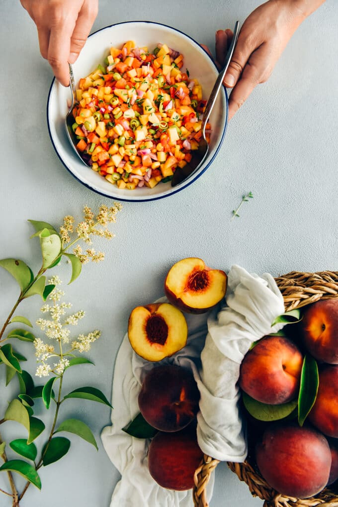 Fresh Corn Peach Salsa is a great recipe to bring summer on your table. Thanks to tangy garden tomatoes, hot peppers and red onion, this is not an overly-sweet salsa. Perfect on chips, chicken, fish or even in sandwiches. #salsa #peachsalsa #salsarecipe #freshpeach #partyfood 用手在白色的碗里搅拌新鲜的玉米桃酱