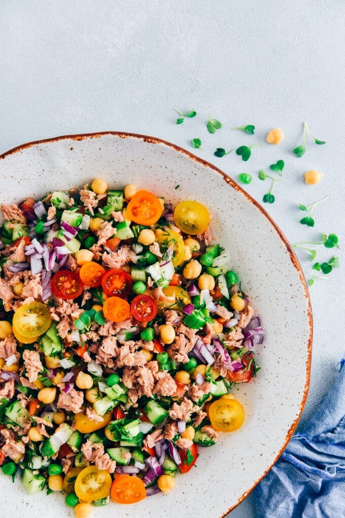 Chickpea Tuna Salad Recipe with a shallot vinaigrette is full of amazing flavors. Packed with protein, fibre and fresh ingredients, this salad is healthy, tasty and keeps you full until dinner time. #tunasalad #chickpeasalad #healthyeating 白碗里的鹰嘴豆金枪鱼沙拉配西红柿和黄瓜。