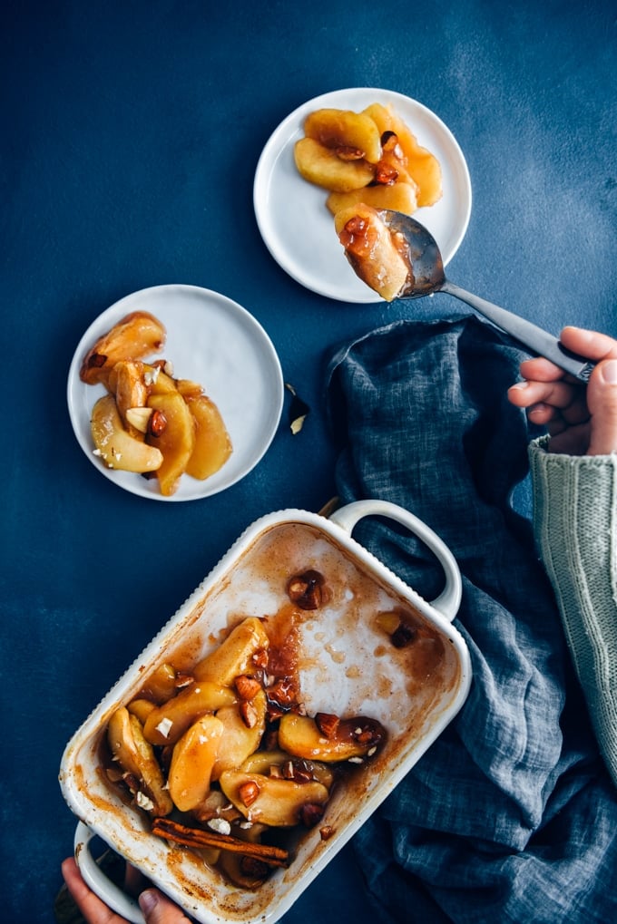 These cinnamon baked apple slices are like the gluten-free and vegan version of apple pie. Way easier to make! A perfect light dessert for fall. #applerecipe #falldessert #bakedappleslices 手端着白色盘子里的烤苹果片