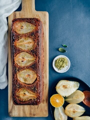 木板上放着梨面包，旁边放着焦糖梨和用铁锅盛着的楔形橘子。