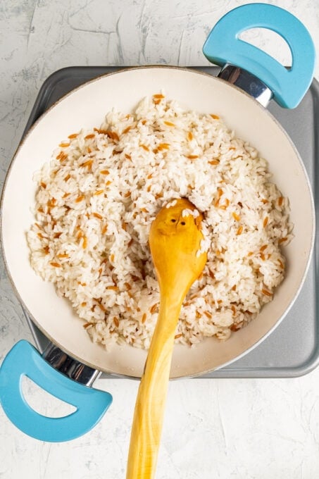 棕色的意大利面和米饭放在一个白色的平底锅里，里面放着一把木勺。