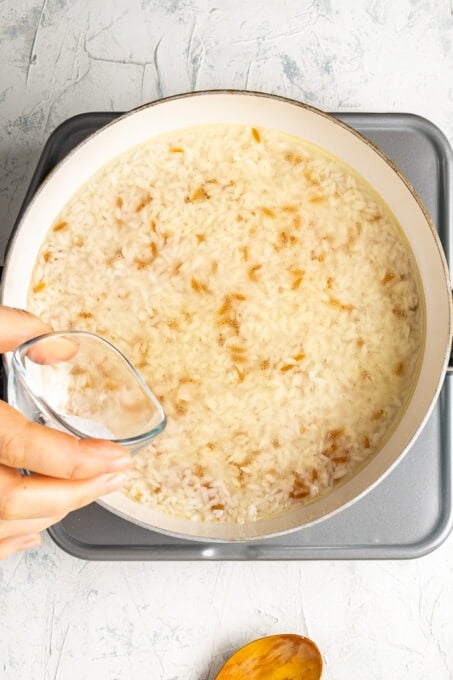 一只手把水倒在炉子上的白色锅里的米饭上。