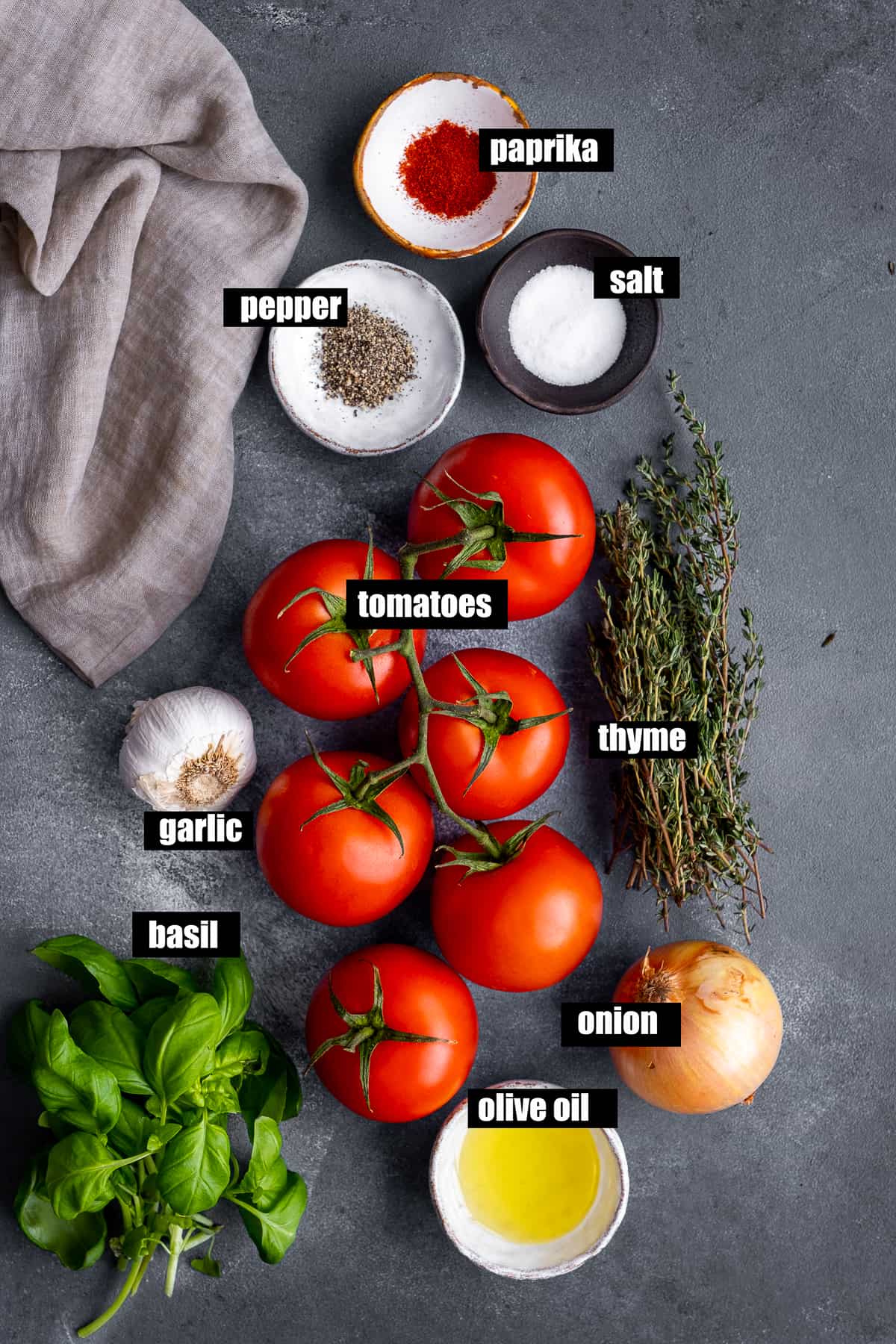 西红柿、洋葱、大蒜、油、罗勒、百里香、辣椒粉、盐和胡椒在深灰色的背景上。