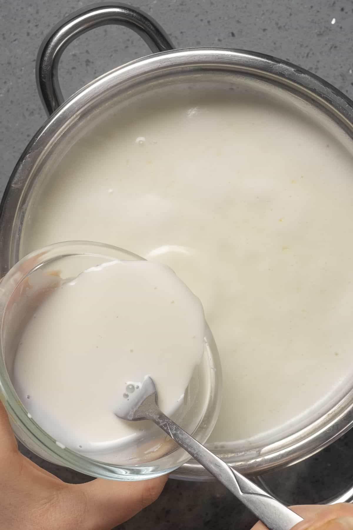 用手将牛奶和玉米淀粉的混合物倒入沸腾的牛奶中。