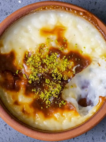 Rice pudding with a golden top garnished with pistachios in a clay bowl.