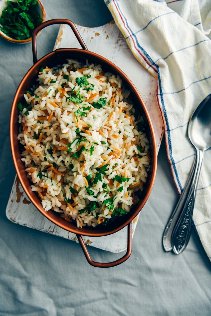 This Rice Pilaf With Orzo is my ultimate side dish that pairs well with anything. Perfectly fluffy every time! #ricerecipe #ricepilaf #sidedish #vegetarianside 米饭饭配意大利面,用铜锅盛着,旁边放着两把勺子。